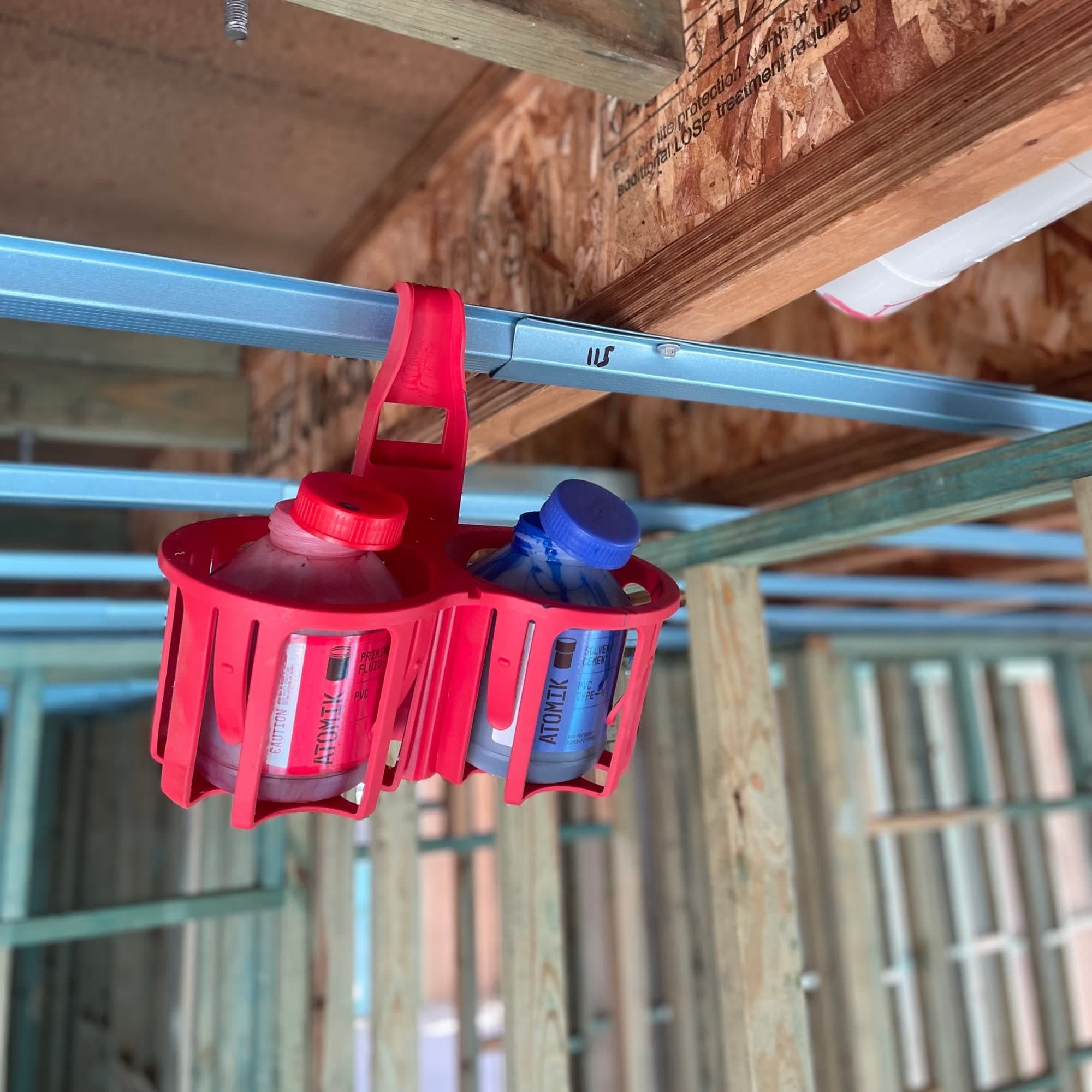 Red bottle holder with two bottles hanging from a metal beam in a construction setting.